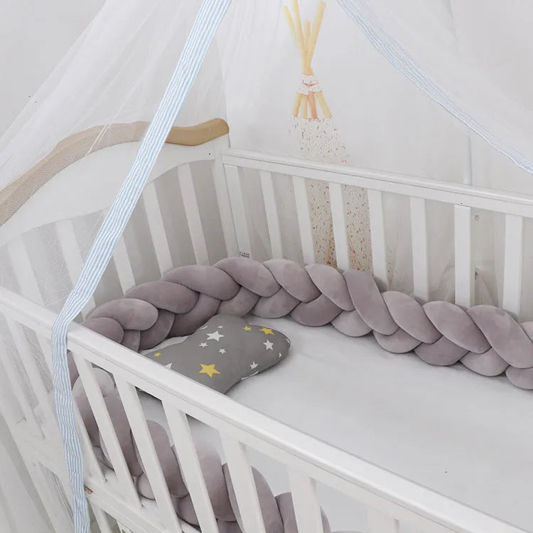 Braided knot style crib bumper in spandex velvet, wrapped around white cot rails in a nursery.