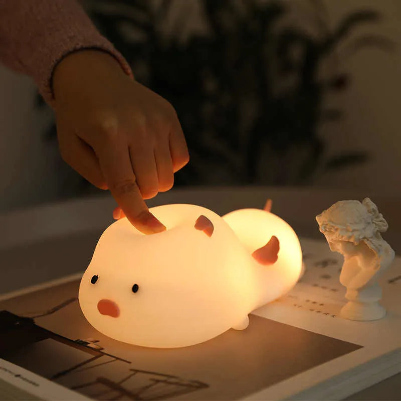 Pink silicone night light in the shape of a sleeping pig on a table.
