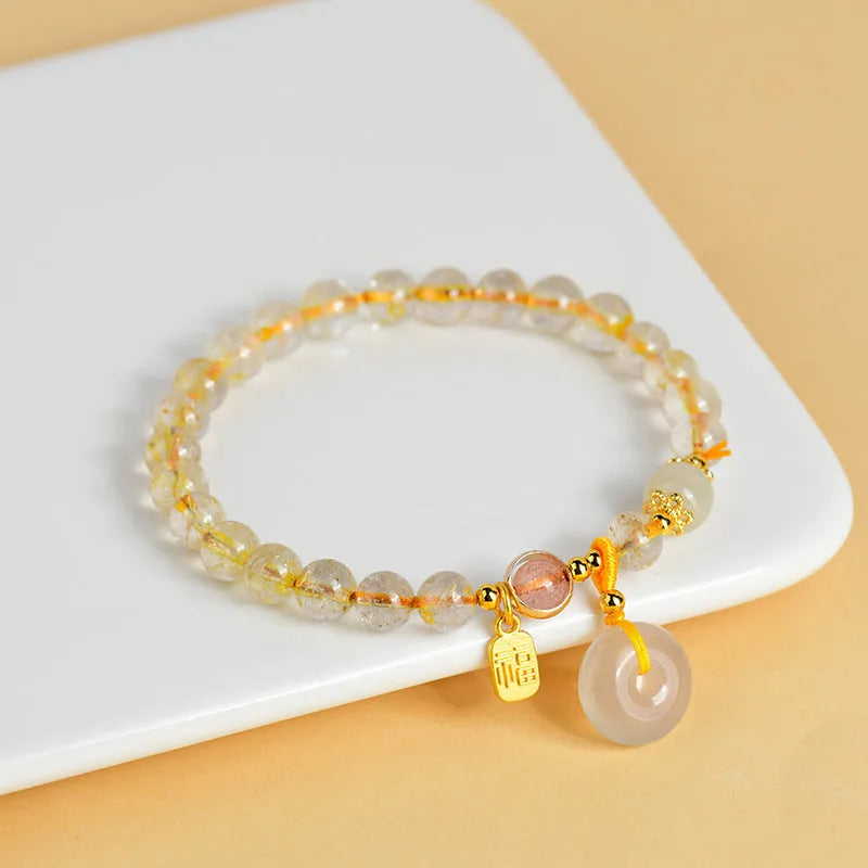 Gold rutilated quartz bracelet with a peace buckle pendant and geometric safety clasp.