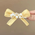 Yellow cloth bow barrette with rhinestones and a pearl on a plastic duckbill hair clip.