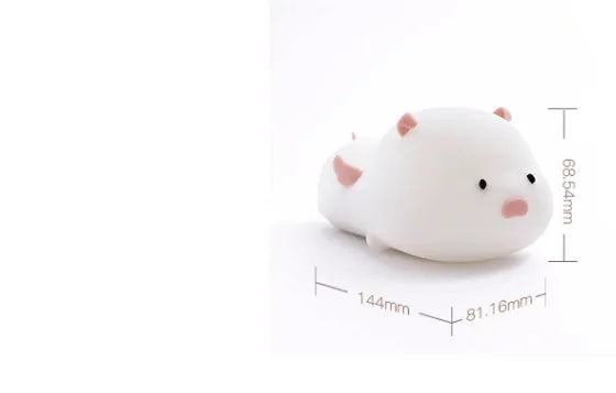 Pink silicone night light in the shape of a sleeping pig on a table.