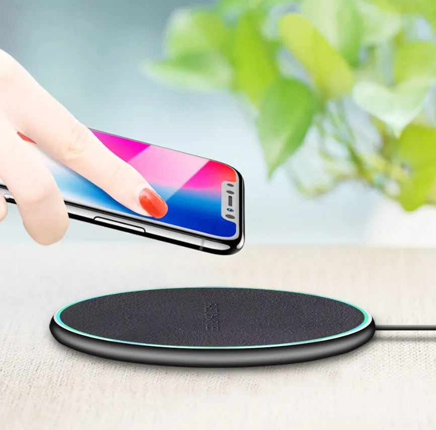 Black circular Qi wireless charging pad for iPhone 11 on a desk.