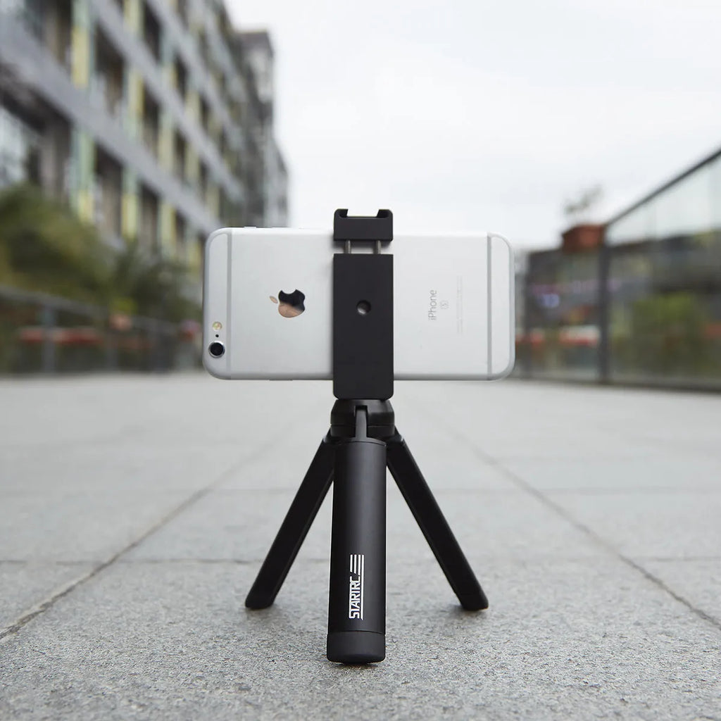 Silver aluminium alloy phone bracket for iPhone shown in clip and tripod style next to a mobile phone.