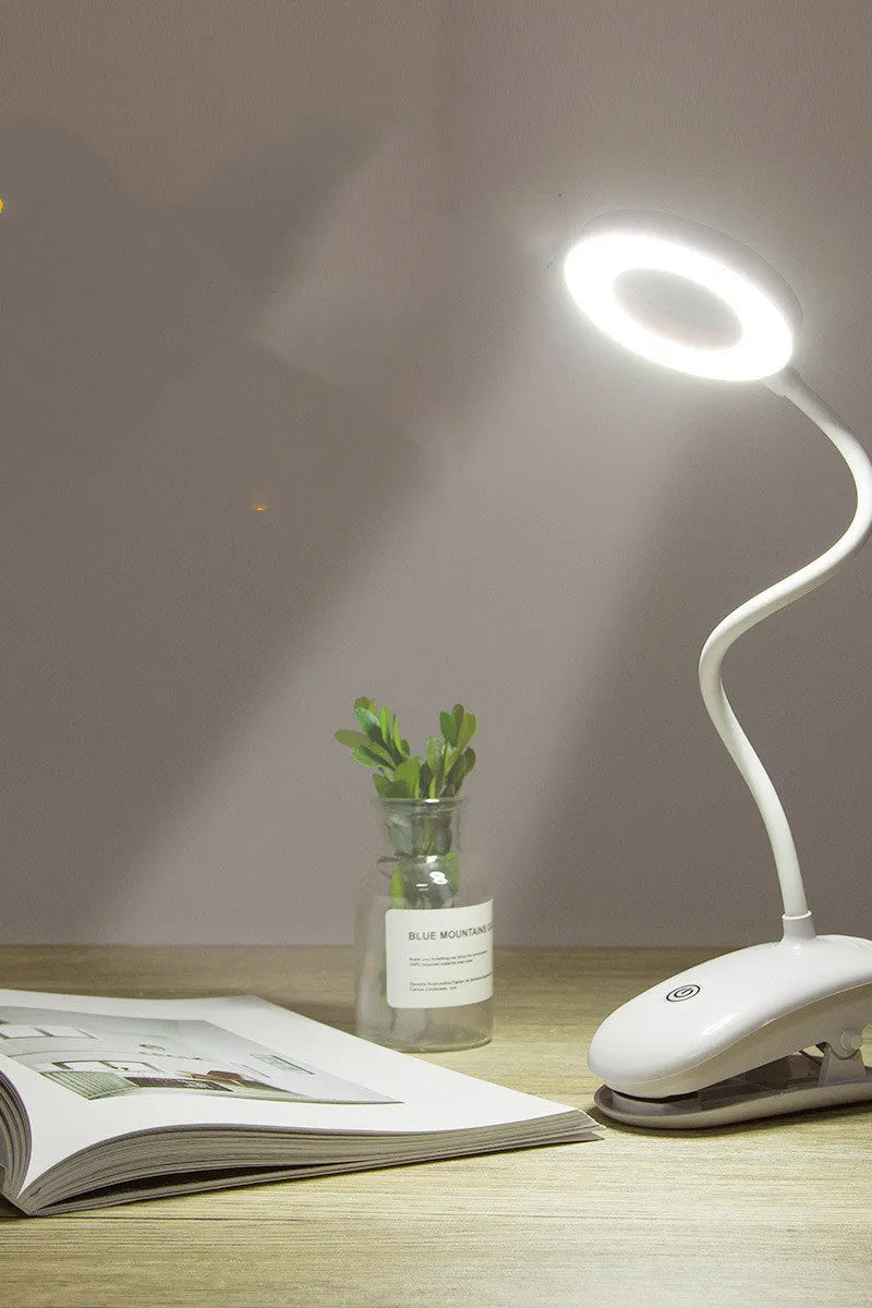 Modern clip-on rechargeable LED desk lamp with touch switch and plastic shade in use on a desk.