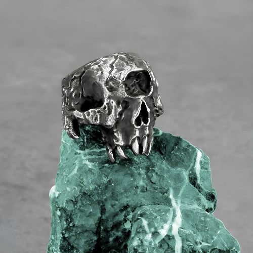 Close-up of a silver-toned alloy ring with a raised one-eyed skull design on a black background.