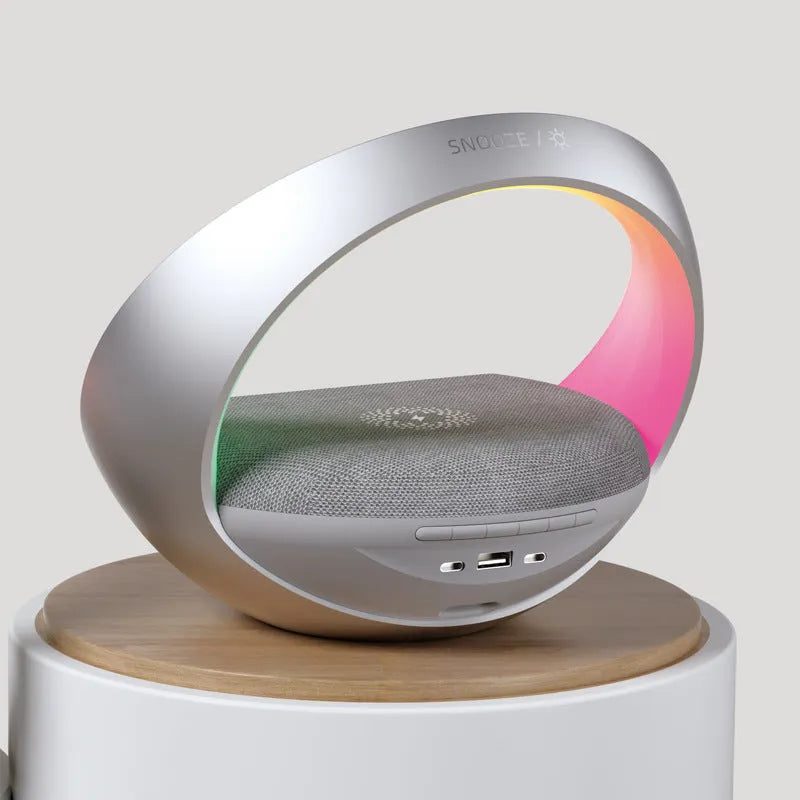 Beige multifunctional Bluetooth speaker with wireless charging surface and ambient LED lighting on bedside table