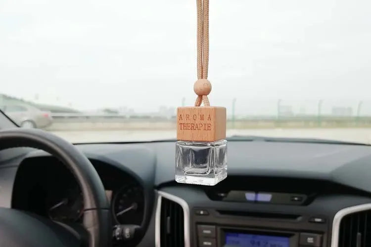 Square clear glass car fragrance pendant bottle with 8ml capacity hanging from a rearview mirror