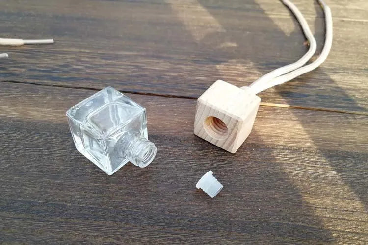 Square clear glass car fragrance pendant bottle with 8ml capacity hanging from a rearview mirror