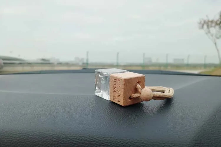 Square clear glass car fragrance pendant bottle with 8ml capacity hanging from a rearview mirror