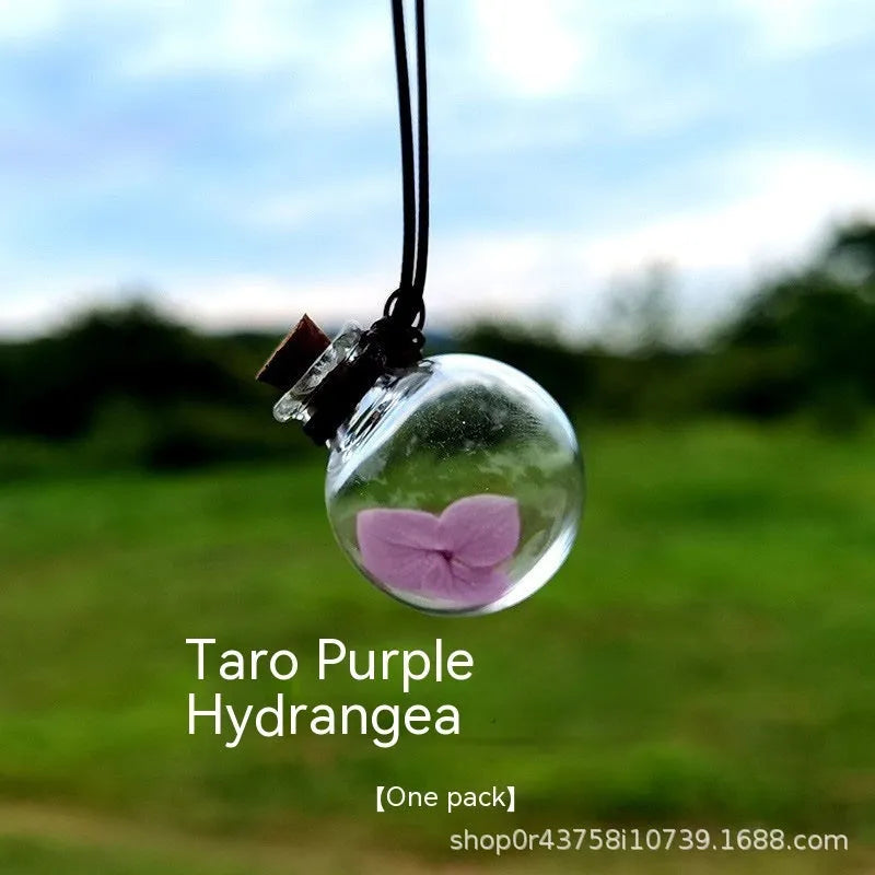Glass car perfume pendant with preserved flowers inside, shown in a selection of different floral colours.