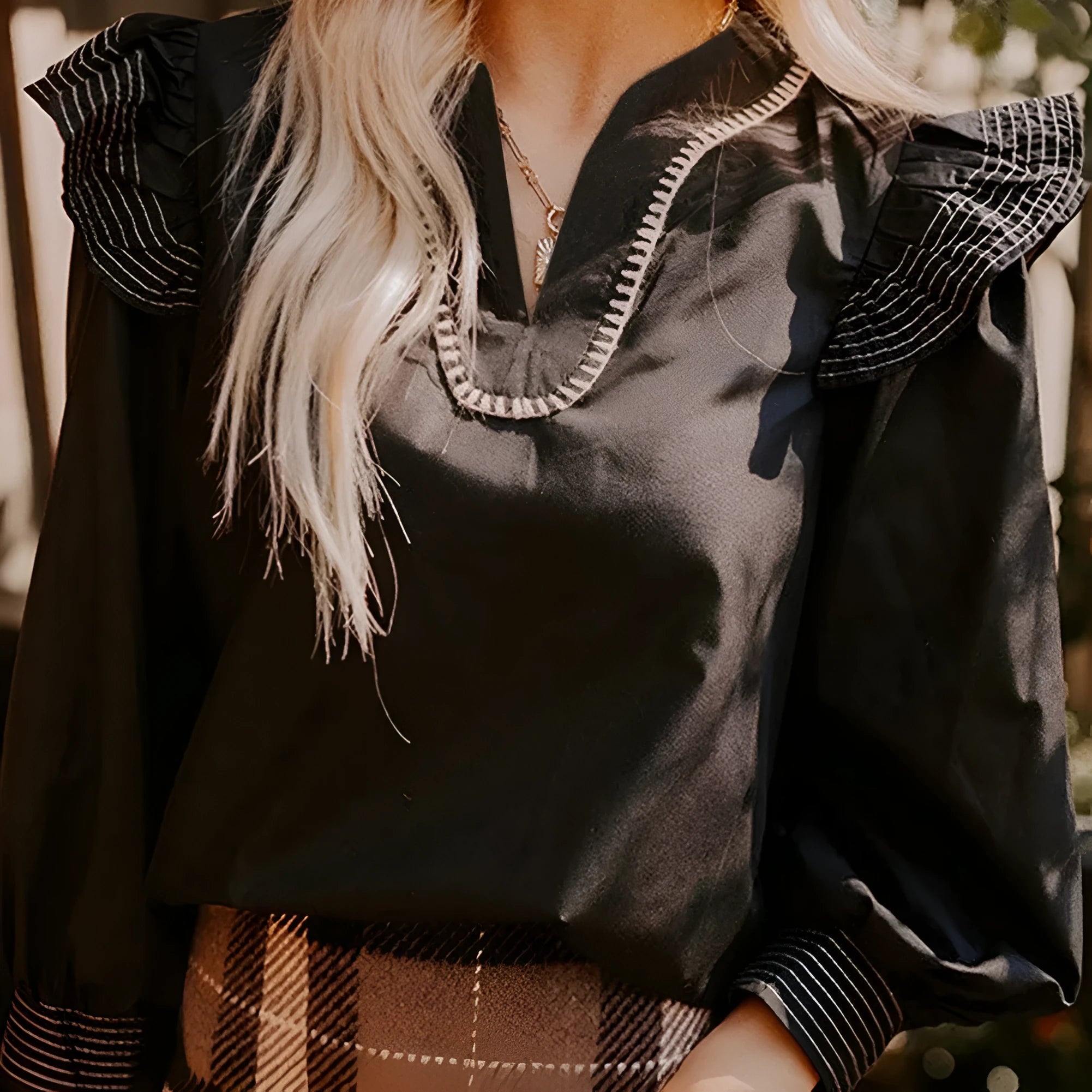 Black long sleeve women's blouse with V-neck, contrast stitching, and ruffle sleeve details.