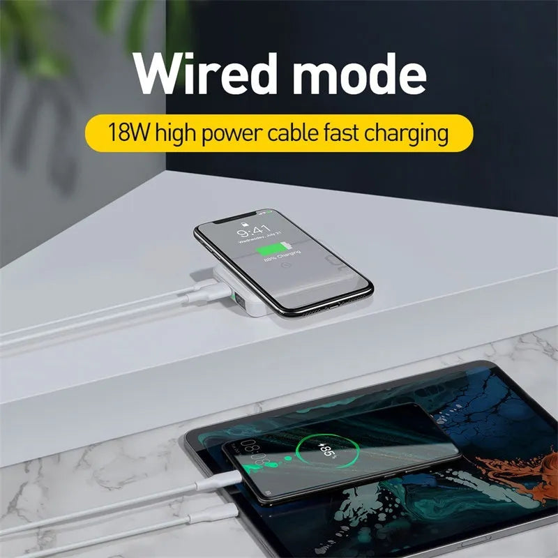 Square black wireless power bank with digital display showing battery percentage, next to a smartphone on its wireless charging surface.