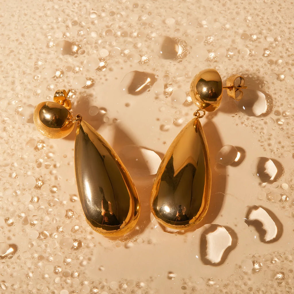 A pair of gold-coloured geometric hemisphere earrings with a hanging water droplet pendant.