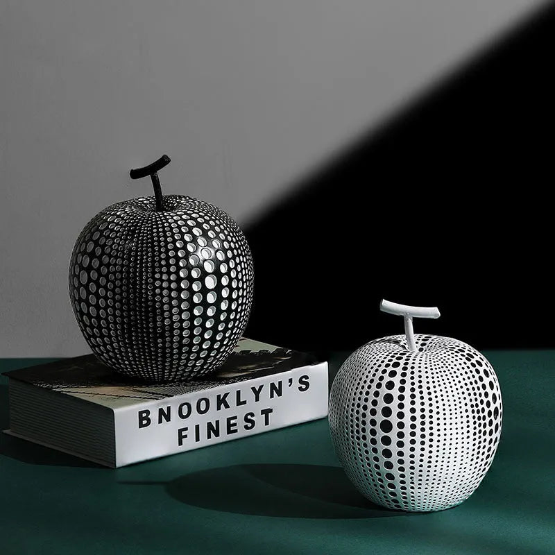 A tall black resin vase and a low white resin apple decoration on a wooden table.
