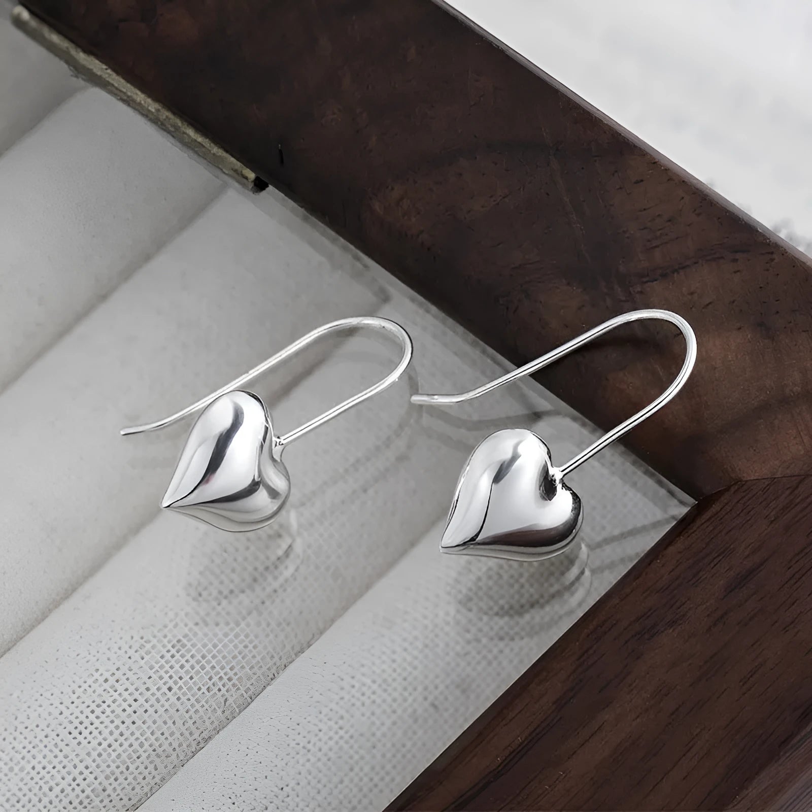 Silver glossy heart-shaped Korean-style earrings with a three-dimensional design on a white background.
