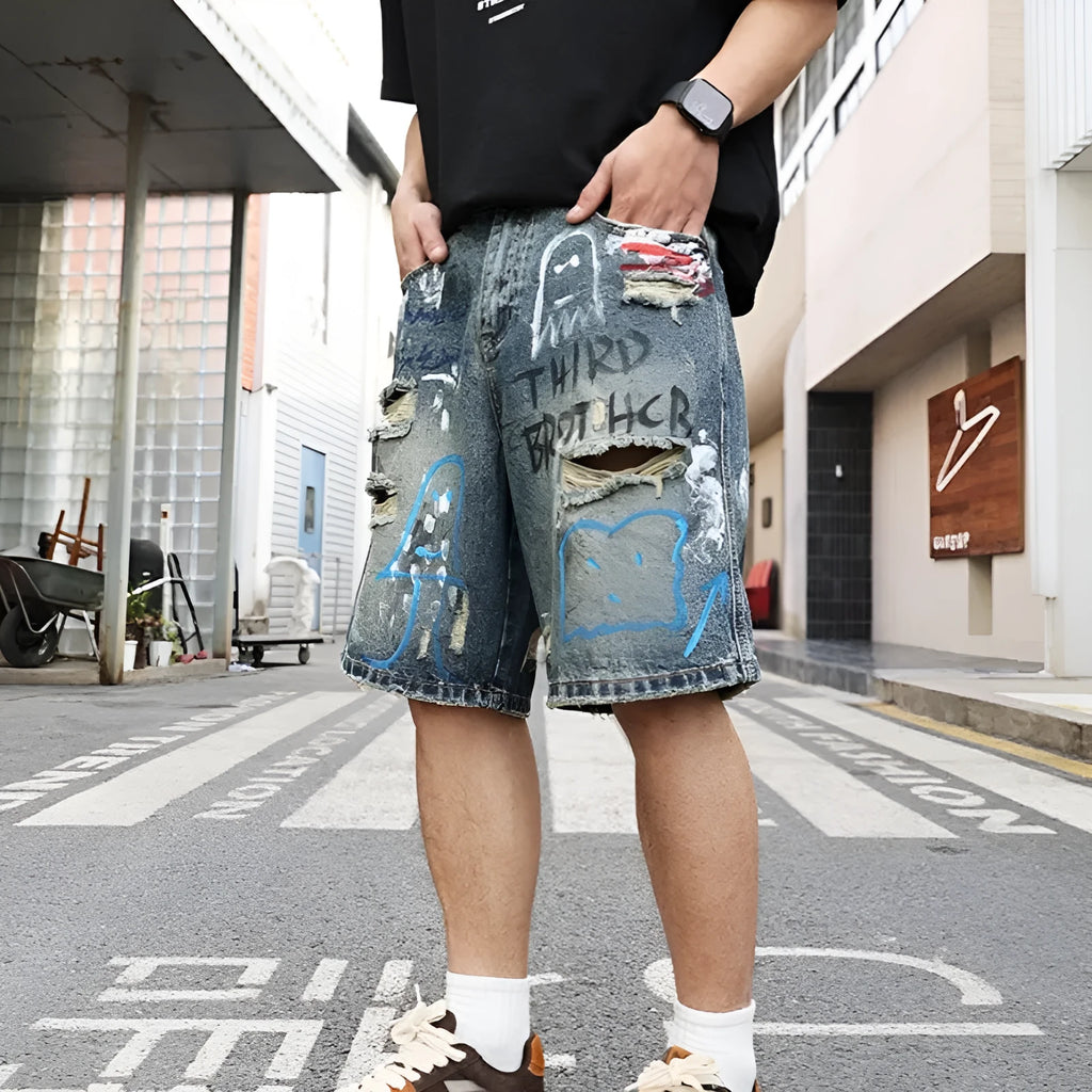 Blue men's ripped denim shorts with graffiti style and straight leg cut on a hanger.