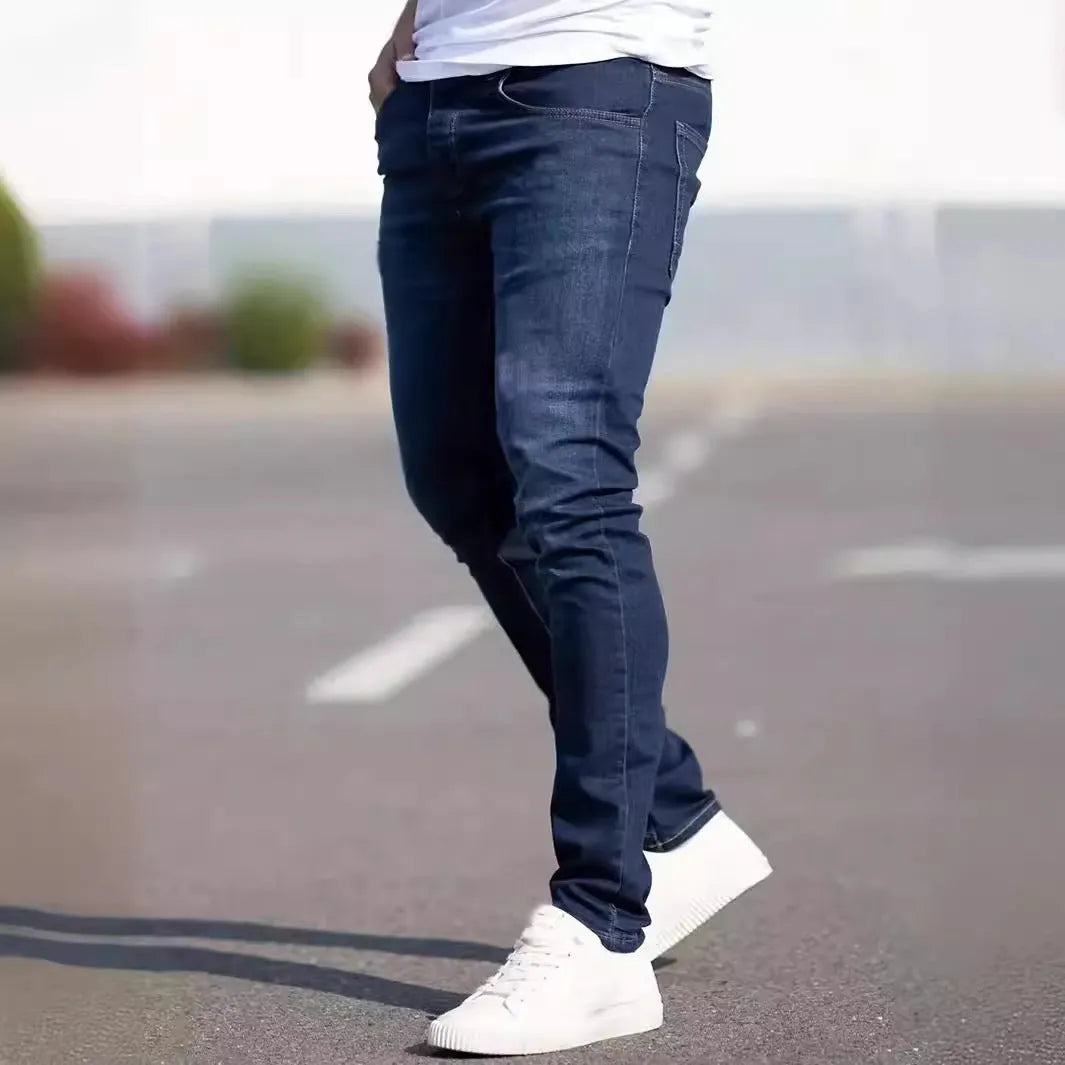 Men's dark blue slim-fit skinny jeans with a zip fly and mid-rise waist on a plain background.