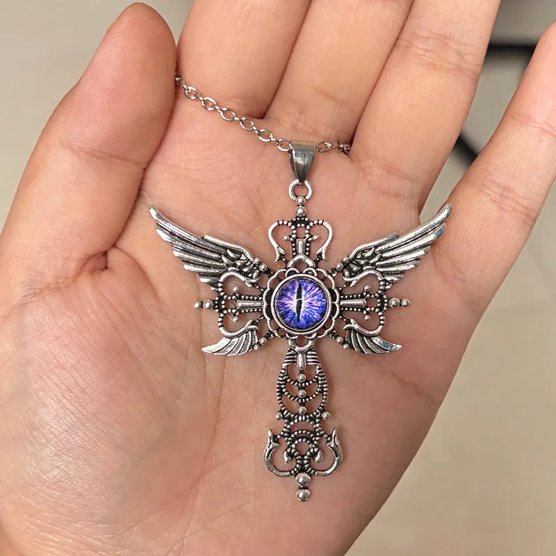 Close-up of a silver-coloured geometric pendant with wing details and a central cross on a chain.