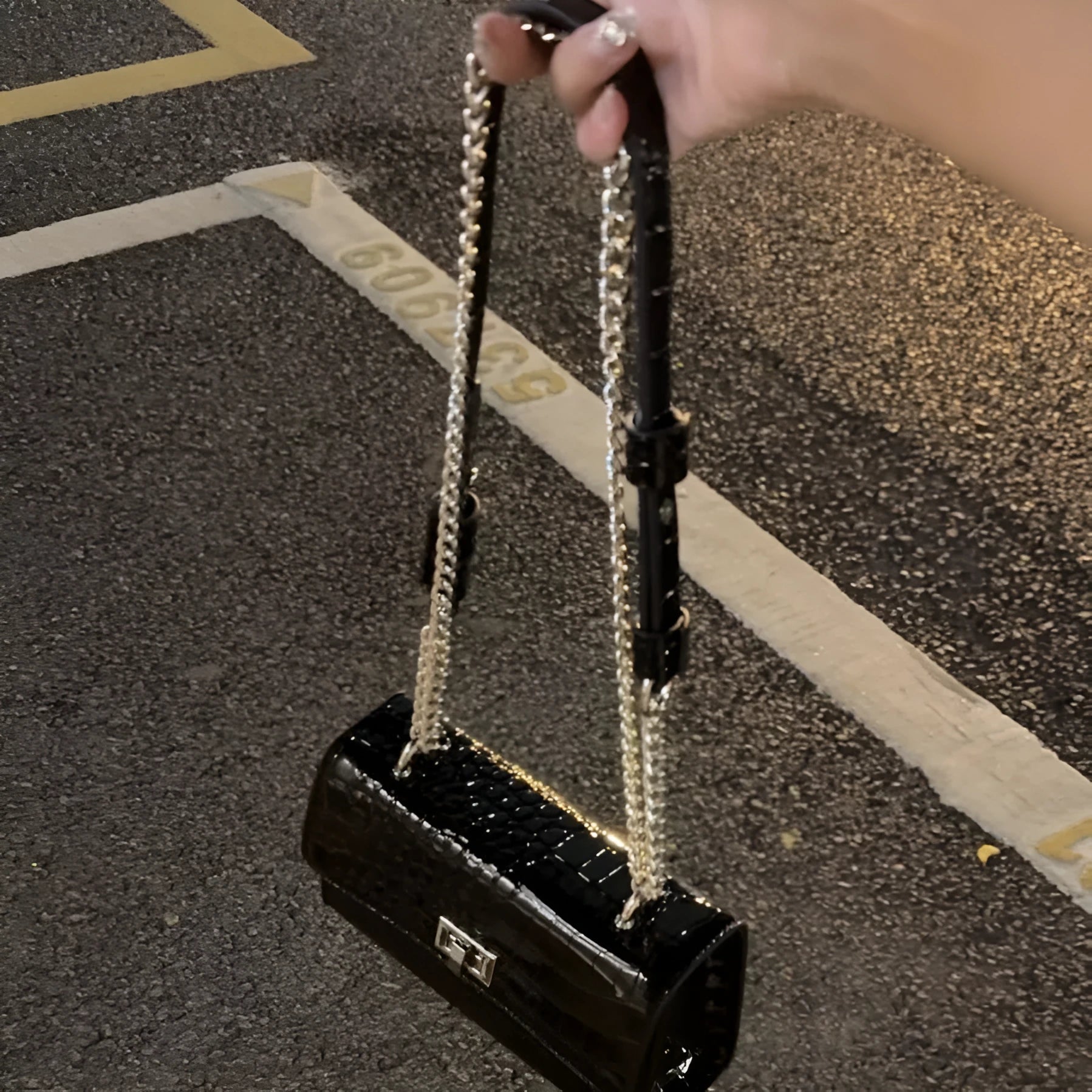 Small square black crossbody bag with chain strap and bow tie detail on urban background