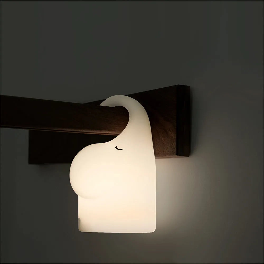 White silicone elephant-shaped night light with a warm glow on a bedside table.