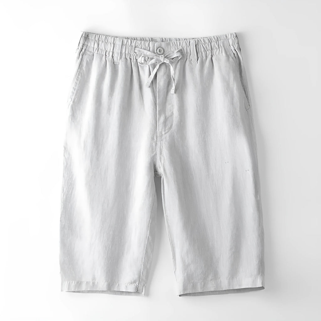 Man wearing light grey linen capri trousers with a loose, straight-leg fit on a beach.