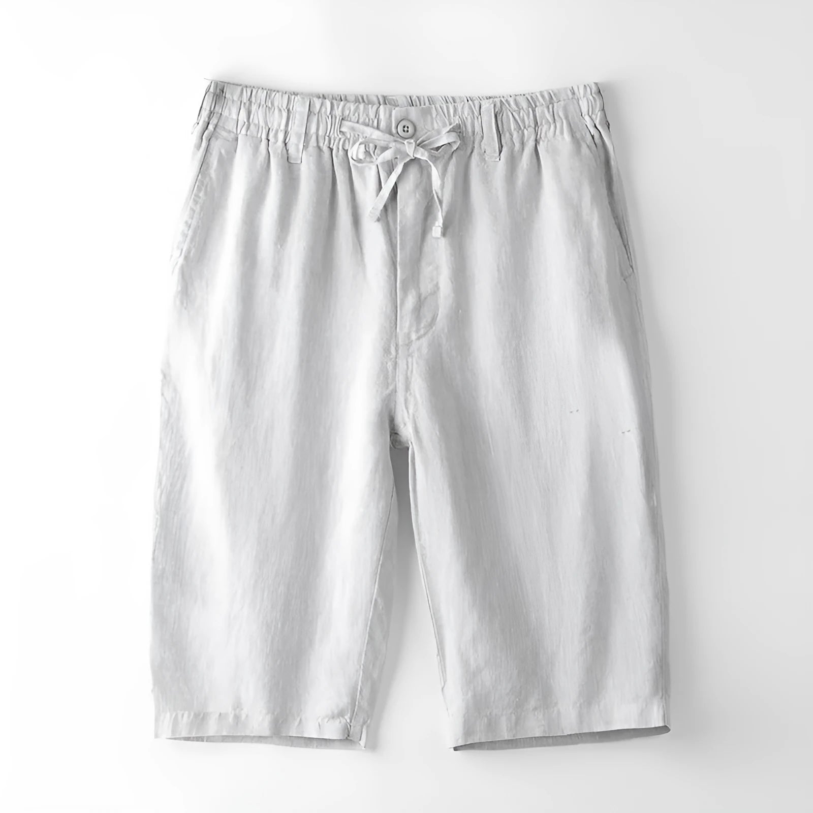 Man wearing light grey linen capri trousers with a loose, straight-leg fit on a beach.