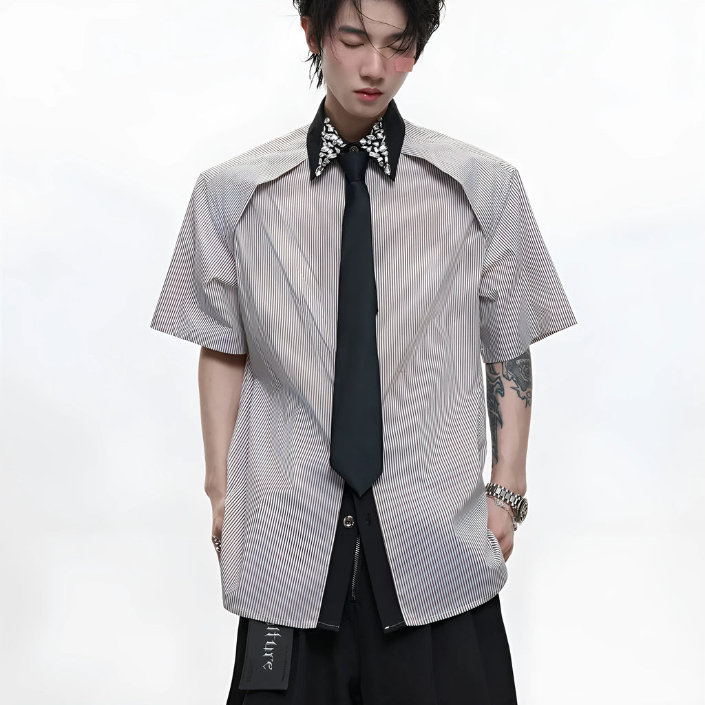 Man wearing a blue loose fit shirt with patchwork stripes, a diamond tie detail, and a flip collar.