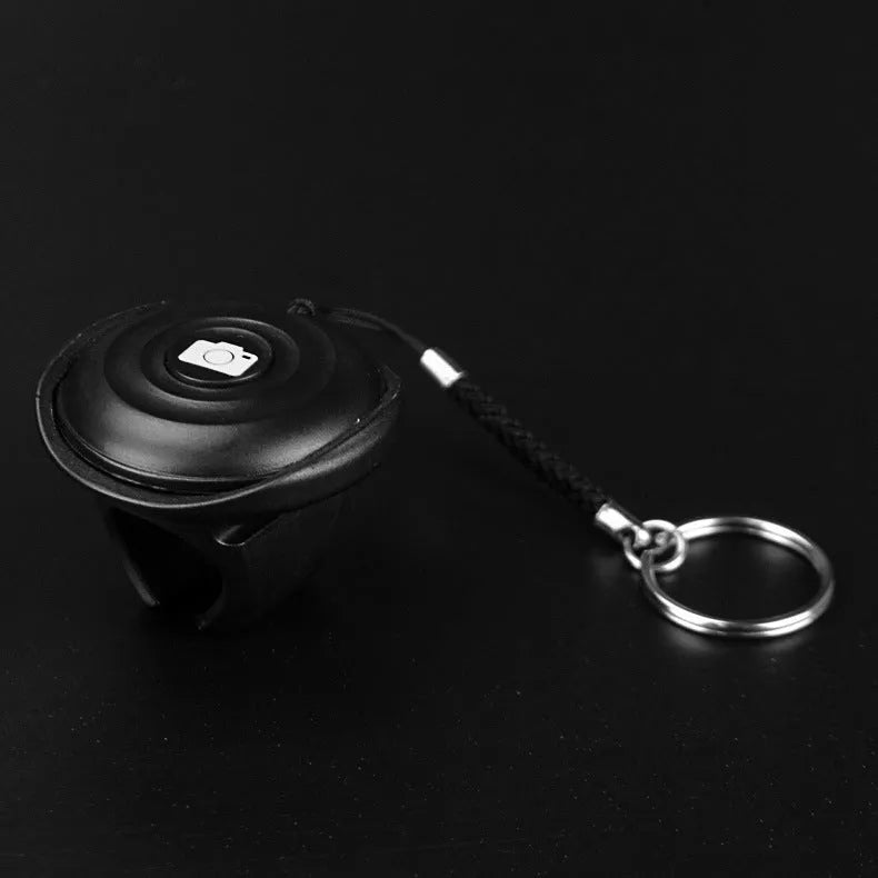 Small black Snap Bluetooth remote shutter next to a smartphone on a tripod, demonstrating wireless camera control.