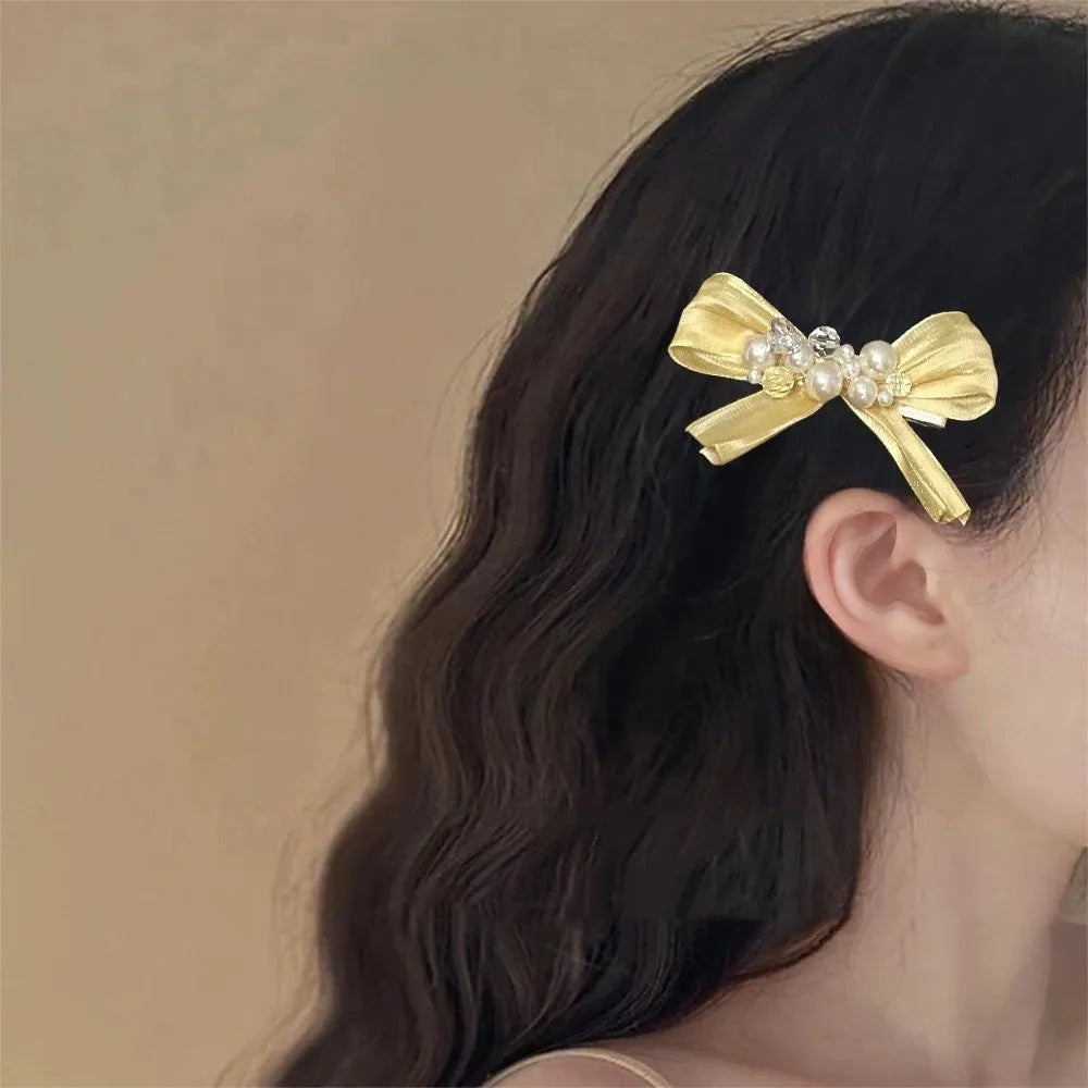 Yellow cloth bow barrette with rhinestones and a pearl on a plastic duckbill hair clip.
