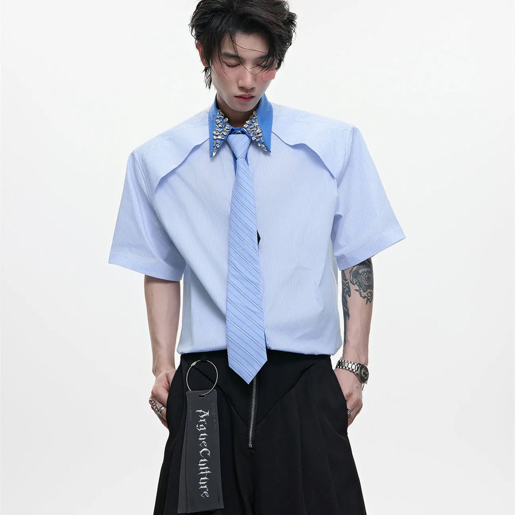 Man wearing a blue loose fit shirt with patchwork stripes, a diamond tie detail, and a flip collar.