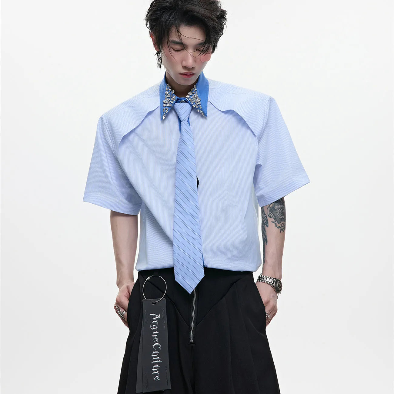 Man wearing a blue loose fit shirt with patchwork stripes, a diamond tie detail, and a flip collar.