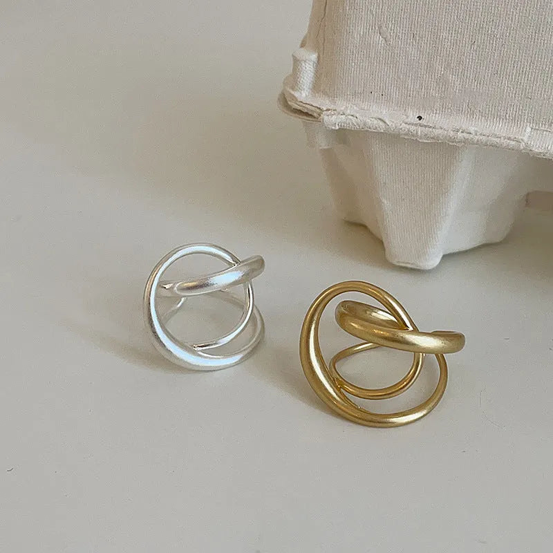 Geometric open ring with interlaced metal design and matte finish in gold colour.