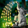 Grey resin elephant garden statue with warm white LED light glowing at its base on a patio.