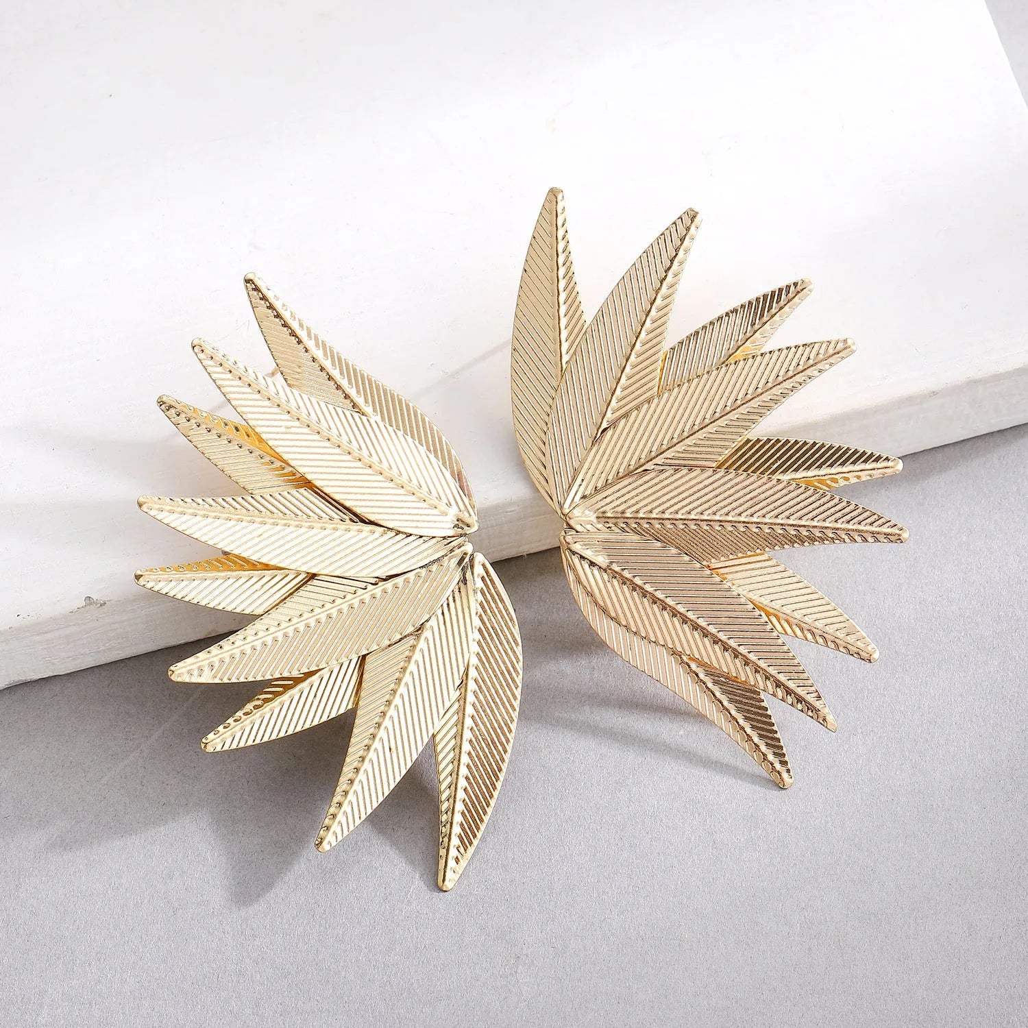 Gold and white alloy leaf-shaped patch earrings on a plain background