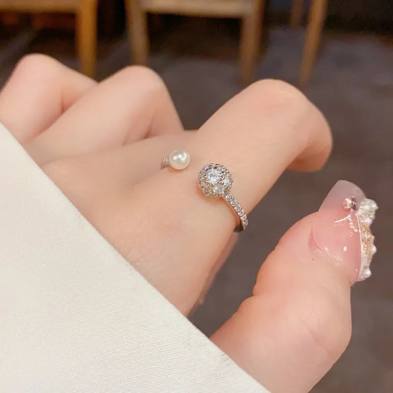 Open-end pearl ring with round zircon stone in gold or silver colour finish.