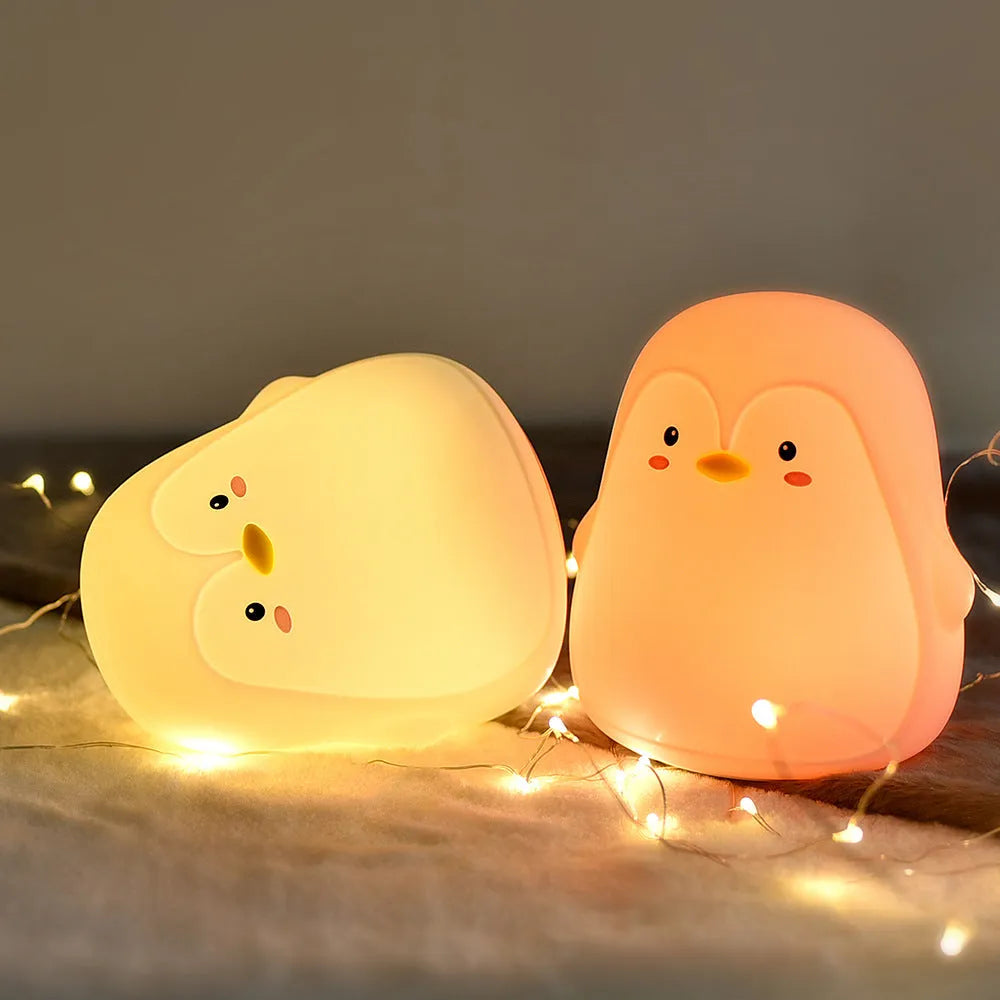 White USB rechargeable penguin-shaped night light with soft glow, shown next to its charging cable.