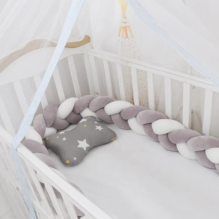 Braided knot style crib bumper in spandex velvet, wrapped around white cot rails in a nursery.