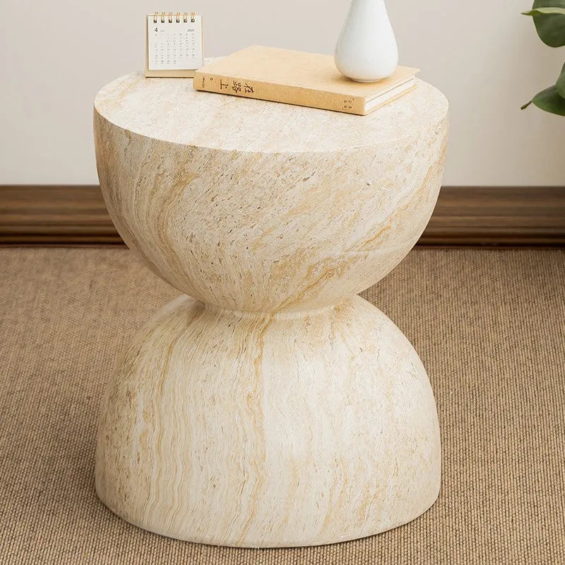 Modern hourglass-shaped tea table in imitation cave stone finish placed beside a sofa in a living room