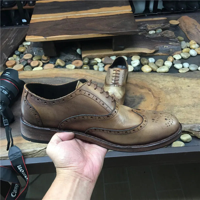 Men's light brown leather lace-up shoes with hand-carved distressed detailing on a wooden background.