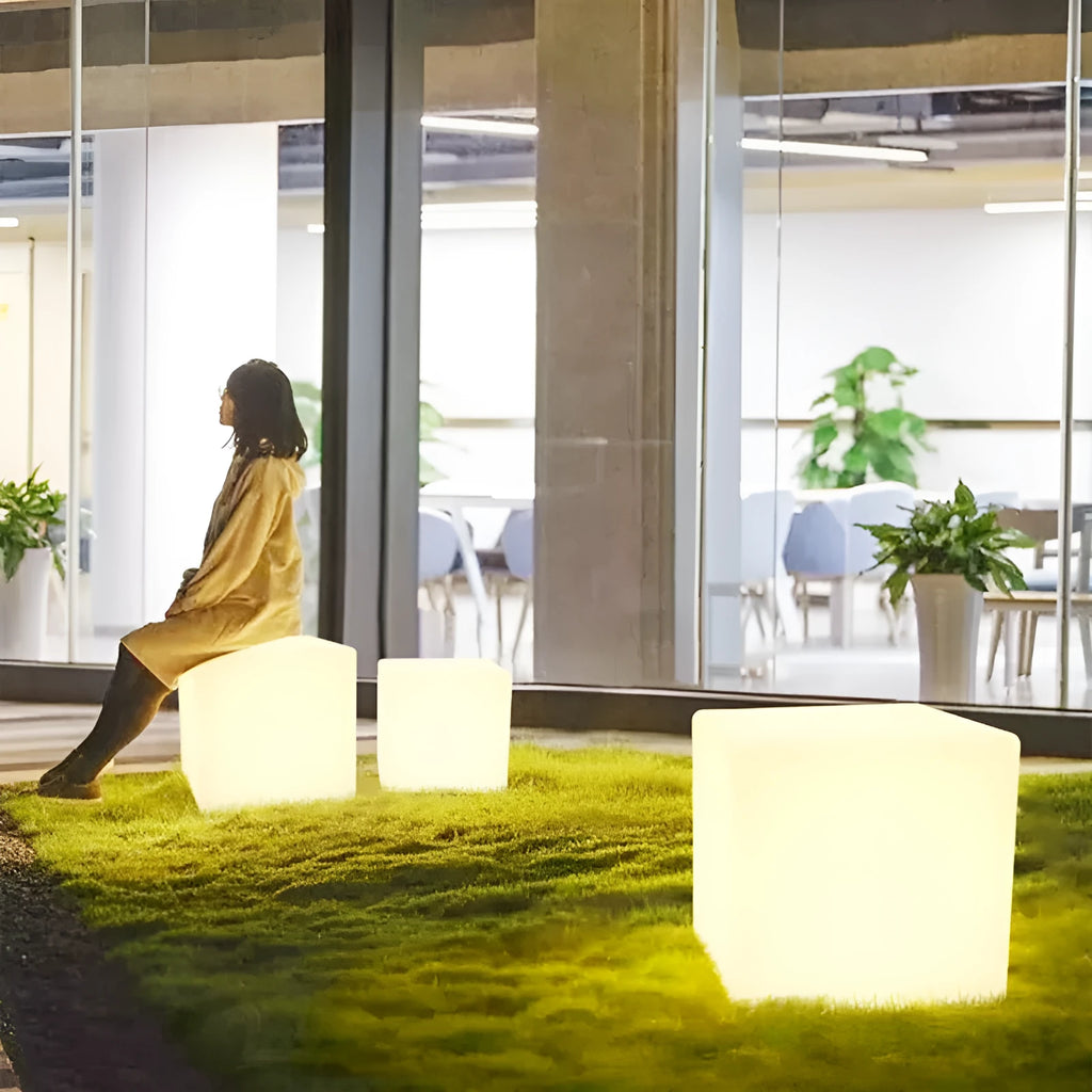 A modern square white LED cube light stool in a garden setting, showing its size options.