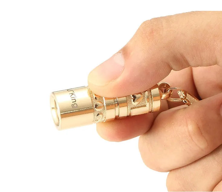 Gold-coloured zinc alloy mini LED flashlight on a keyring for outdoor and emergency use.