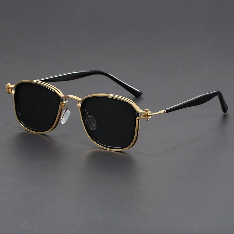 Retro square sunglasses with black gold frames and grey AC lenses on a wooden surface.