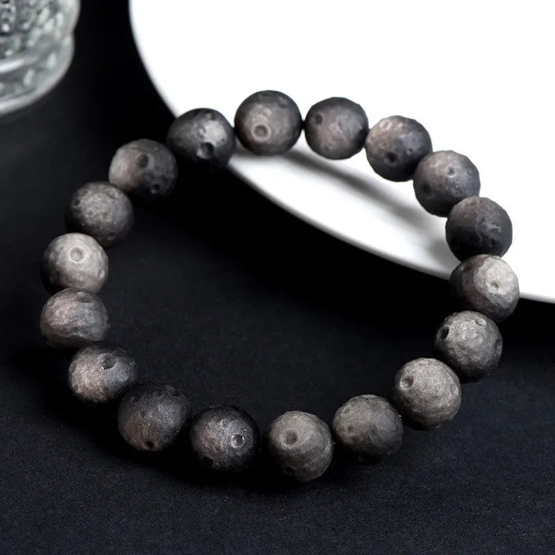 Natural obsidian crater ball bracelet in gold or silver stone colour on a wrist, showing textured bead surface.