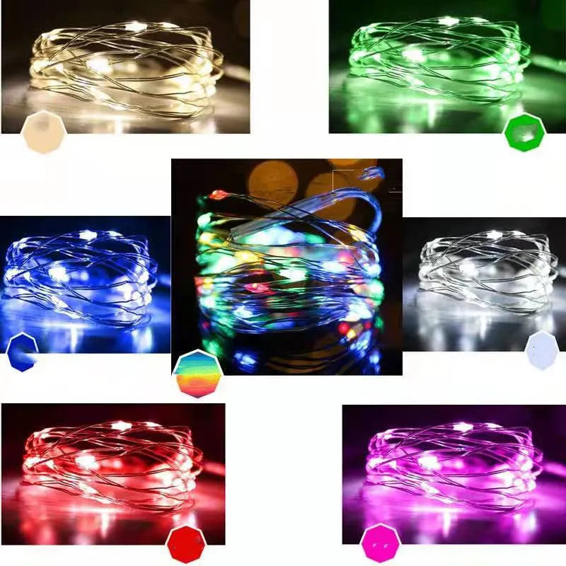 Close-up of bendable copper wire fairy lights with small LEDs, showing battery box and USB cable on a wooden surface.