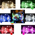 Close-up of bendable copper wire fairy lights with small LEDs, showing battery box and USB cable on a wooden surface.