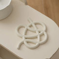 Irregular-shaped ceramic heatproof mat in a solid colour on a wooden table, protecting it from a hot pan.