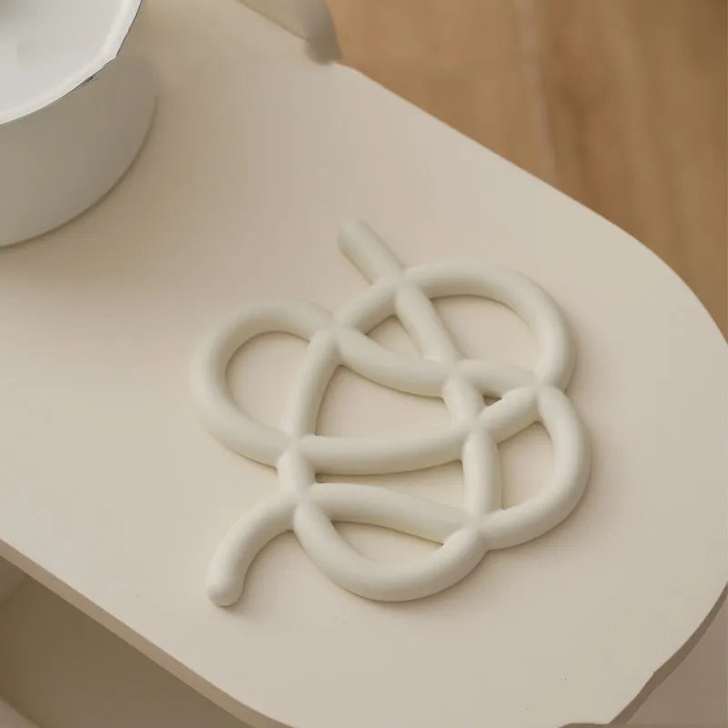 Irregular-shaped ceramic heatproof mat in a solid colour on a wooden table, protecting it from a hot pan.