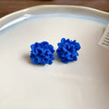 A pair of geometric cloth earrings with a blue resin flower decoration and silver needle detail.