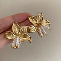 Golden flower-shaped earrings with pearl details on a white background.