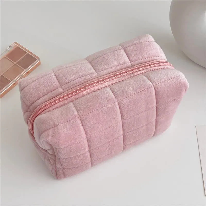 Three plush makeup bags in pink, white, and blue with zippers, laid flat showing front